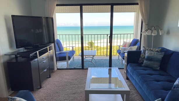 Un salon équipé d’un téléviseur, d’un canapé et d’une table basse, avec vue sur une plage et l’océan.