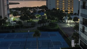 Un complexe hôtelier doté d’une piscine, de courts de tennis et offrant une vue sur l’océan au coucher du soleil.