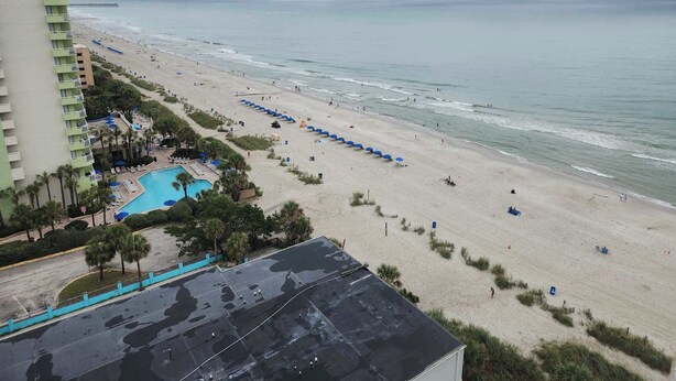 A beach resort with a swimming pool, beach umbrellas, and a pier in the background. - Sea Mist 51508 (Myrtle Beach)