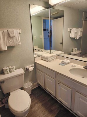 A bathroom with a toilet, sink, mirror, and towels. - Sea Mist 51508 (Myrtle Beach)