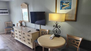 A hotel room with a TV, a desk with drawers, a round table, two chairs, a lamp, and a framed picture on the wall. - Sea Mist 51508 (Myrtle Beach)