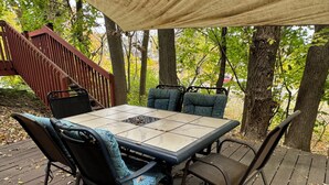 Un espace extérieur aménagé avec une terrasse couverte, comprenant une table et des chaises, entouré d’arbres et d’une plateforme en bois.