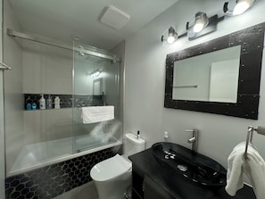 Een moderne badkamer met een glazen douchecabine, een zwart wastafel en een grote spiegel.