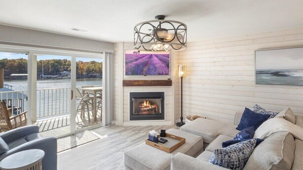 Un salon spacieux avec une cheminée, un balcon offrant une vue sur l’eau et un lustre moderne.