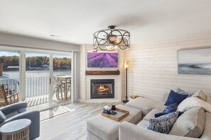 Ein geräumiges Wohnzimmer mit Kamin, ein Balkon mit Blick auf das Wasser und eine moderne Chandelier.