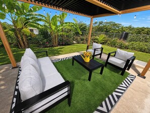 An outdoor patio with a black metal table, white cushioned chairs, and a yellow watering can.