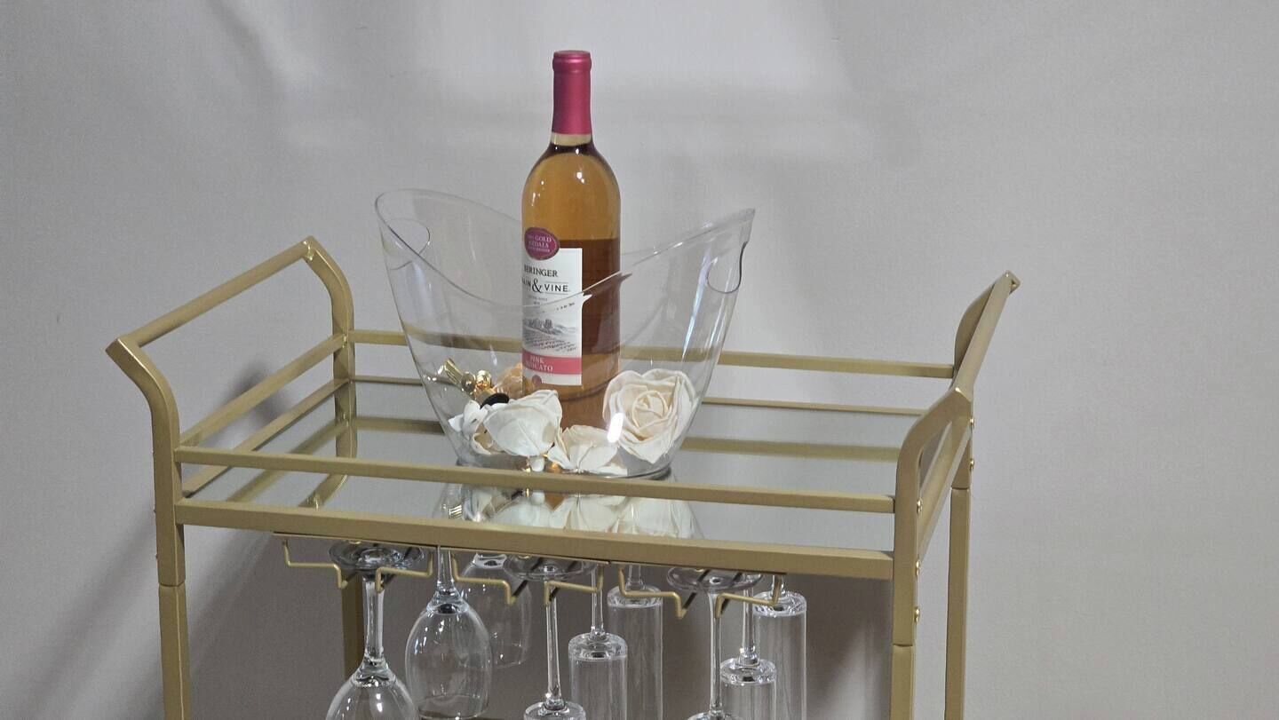 A wine bottle on a metal cart with glasses and flowers.