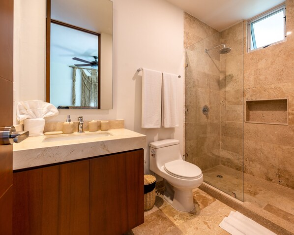 Un baño moderno con lavamanos de mármol, inodoro y ducha con mampara de vidrio.