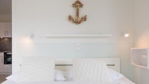 A modern bedroom with a white bed, a decorative anchor on the wall, and a kitchen visible in the background. - Cosy apartment for 3 people with WIFI, TV and balcony (Husum)
