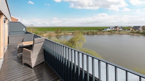 A balcony with wicker furniture overlooking a lake and a distant village. - Cosy apartment for 3 people with WIFI, TV and balcony (Husum)