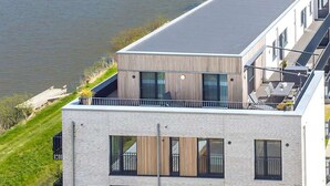 A modern multi-story building with large windows and a flat roof, adjacent to a body of water. - Cosy apartment for 3 people with WIFI, TV and balcony (Husum)
