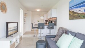 A modern living room with a grey sofa, a flat-screen TV, and a dining area with bar stools. - Cosy apartment for 3 people with WIFI, TV and balcony (Husum)