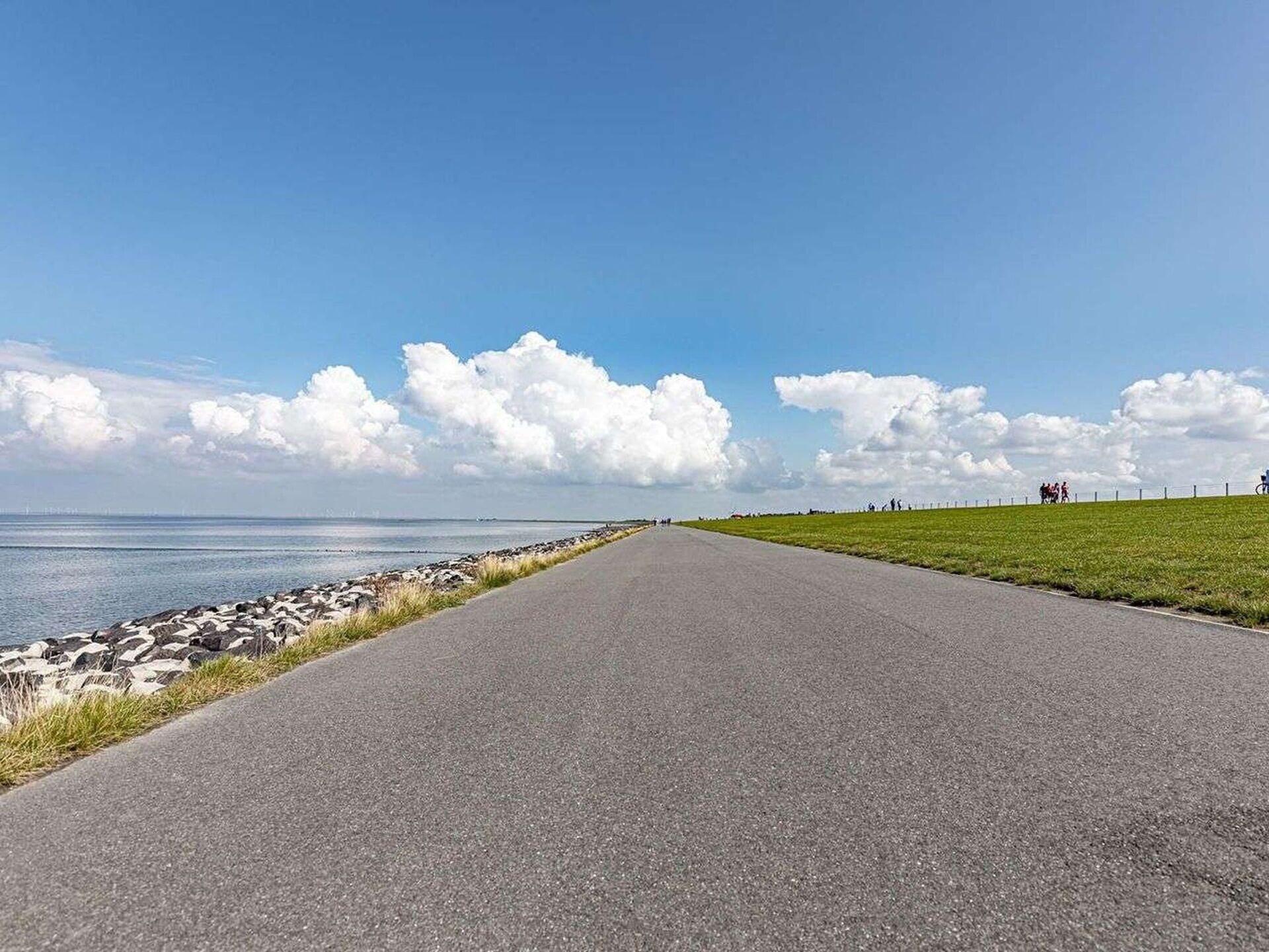 A paved road with a grassy area on one side and a rocky shoreline on the other.
