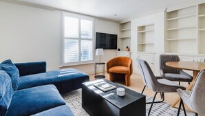 A modern living room with a sofa set, a coffee table, a TV, and a dining area with chairs and a table. - Airy S Kensington 2BR w/ Doorman & Balcony, nr Museums, by Blueground (London)
