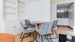 A modern kitchen with white cabinets, a round wooden table, and two grey upholstered chairs. - Airy S Kensington 2BR w/ Doorman & Balcony, nr Museums, by Blueground (London)