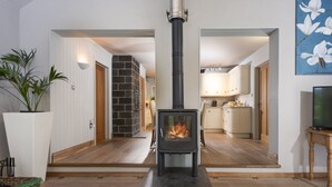 A living room with a wood-burning stove, wooden flooring, a potted plant, and a television on a wooden stand. - Tucked away in a magical corner of Cornwall, South Lodge sits peacefully on the enchanting Bonython (Helston)
