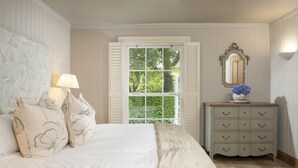 A bedroom with a large bed, a dresser, a mirror, and a window with shutters. - Tucked away in a magical corner of Cornwall, South Lodge sits peacefully on the enchanting Bonython (Helston)