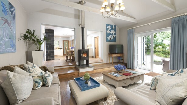 A spacious living room with a fireplace, sofas, a coffee table, and a television. - Tucked away in a magical corner of Cornwall, South Lodge sits peacefully on the enchanting Bonython (Helston)