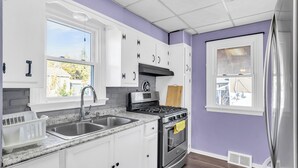 A kitchen with white cabinets, a stainless steel sink, a stove, and a window with a view of the outside.