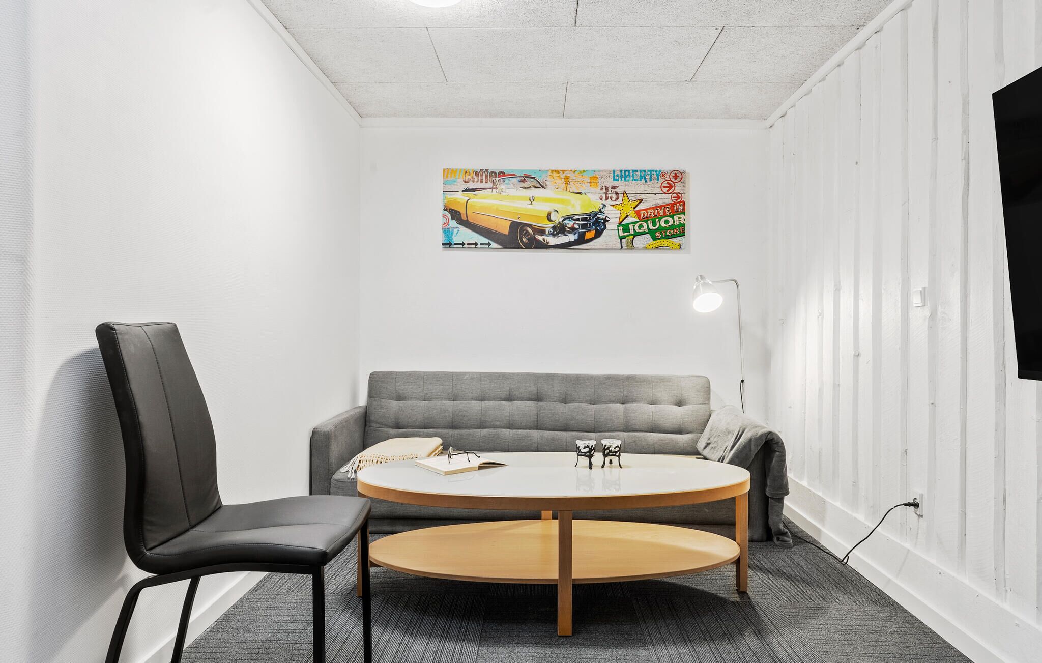 Une pièce avec un canapé gris, une chaise noire et une table ronde en bois.