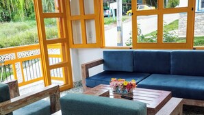 Una habitación con un sofá azul, sillas de madera, una mesita de centro con flores y vistas al exterior.