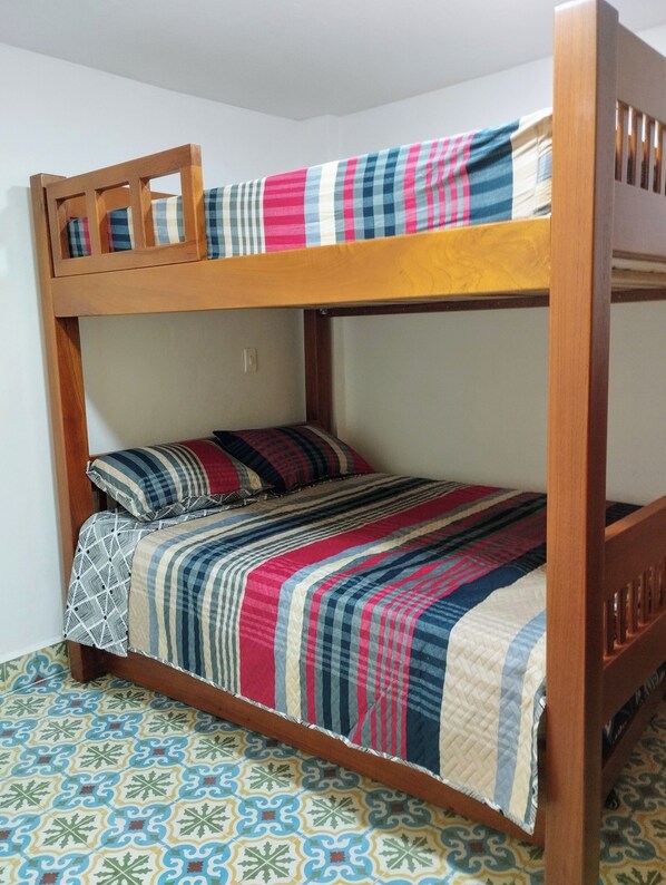 Ein Stockbett mit Holzrahmen und einer farbenfrohen, gesteppten Tagesdecke.