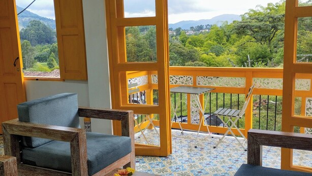 Un balcón con vistas a un paisaje montañoso, mobiliario de madera y suelo de baldosas.
