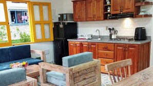 Cocina compacta con armarios de madera, un refrigerador negro, un microondas y una cafetera. Hay una mesa de comedor con sillas y un sofá en la zona de estar.