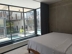 A bedroom with a large window, a bed, and a view of a courtyard. - New, Modern Loft in Main Avenue Tulum (Tulum)