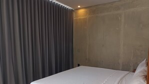 A bedroom with a bed, grey curtains, and a concrete wall. - New, Modern Loft in Main Avenue Tulum (Tulum)