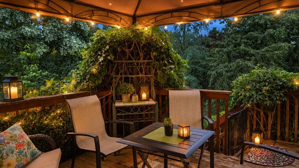 Un área de estar al aire libre cubierta, con una mesa y sillas, rodeada de vegetación y luces colgantes.