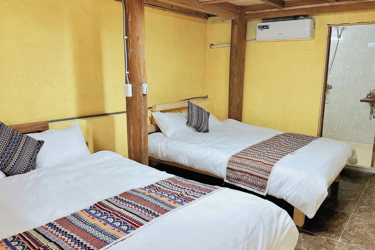 Due letti singoli con coperte a motivi in una stanza dalle pareti gialle e travi in legno.