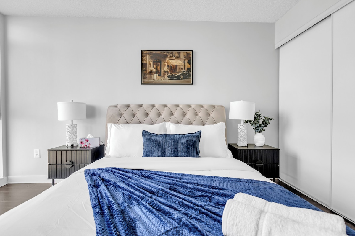 Ett modernt hotellrum med en stor säng, två sängbord, en sänggavel och en inramad tavla på väggen.