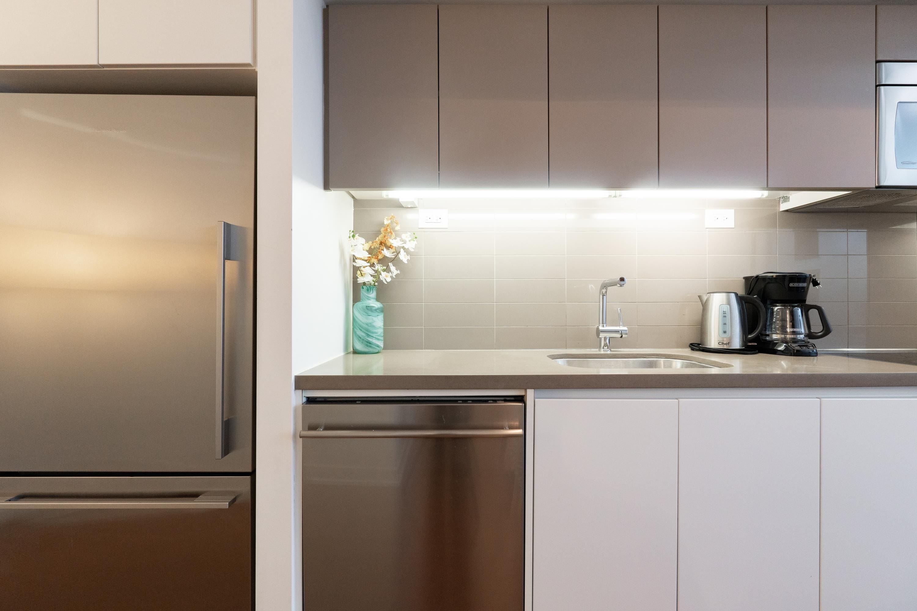 Una cocina moderna con electrodomésticos de acero inoxidable, una cafetera y un florero con flores sobre la encimera.