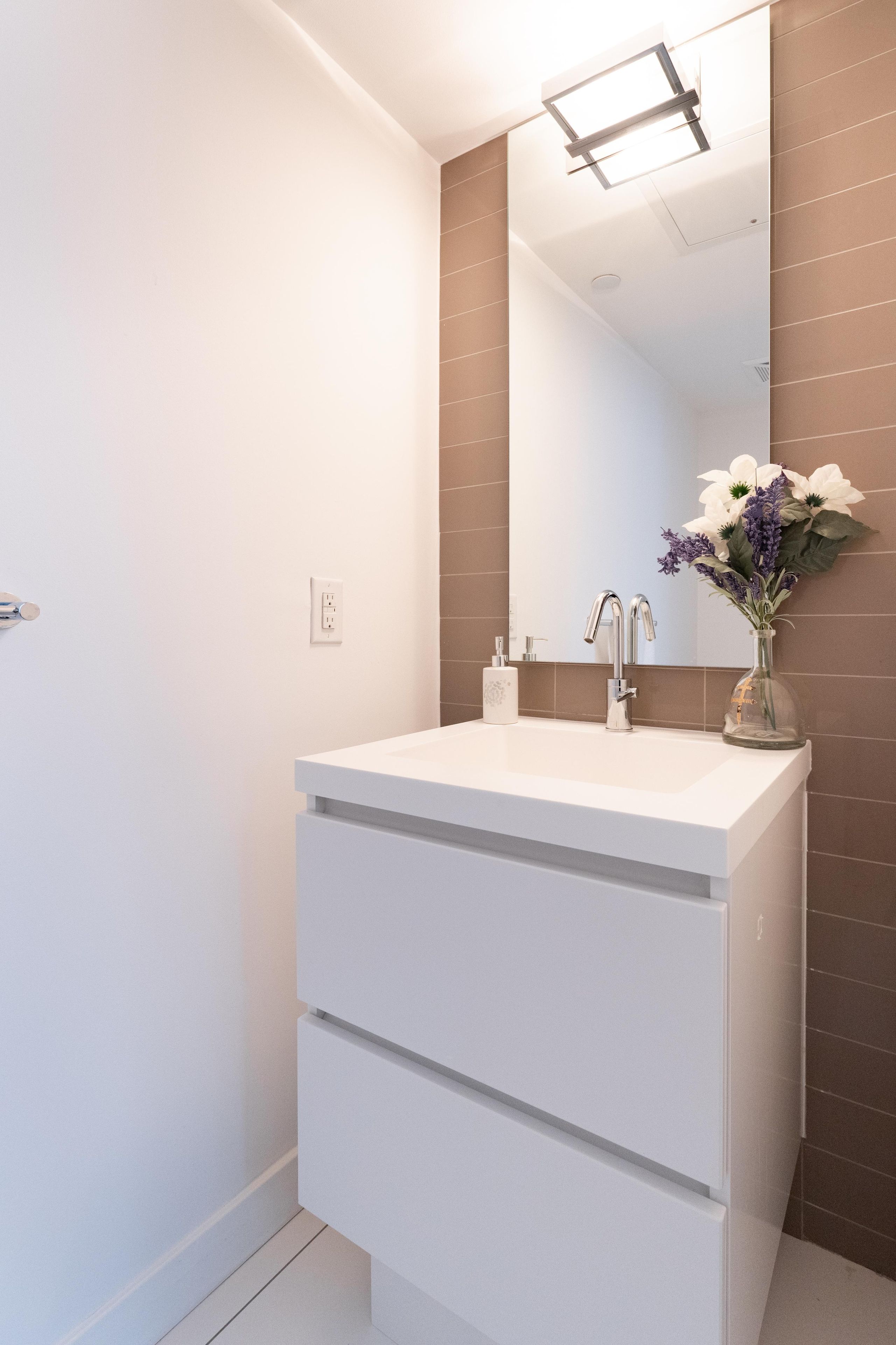 Een badkamer met een wit wastafelmeubel, een spiegel en een vaas met bloemen.