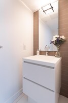 Casa de banho com toucador branco, espelho e um vaso com flores.