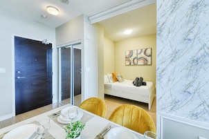 Een moderne hotelkamer met een bed, een eethoek met een tafel gedekt voor twee personen, en een badkamer met een donkere deur.
