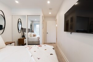 Um quarto com cama, mesa de cabeceira, espelho e guarda-roupa.