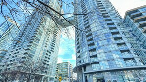 A modern high-rise building with a glass facade, multiple balconies, and a pedestrian walkway. - Panorama Suites-Fort York (Toronto)