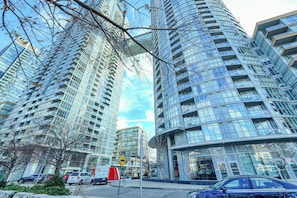 A modern high-rise building with a glass facade, multiple balconies, and a pedestrian walkway. - Panorama Suites-Fort York (Toronto)