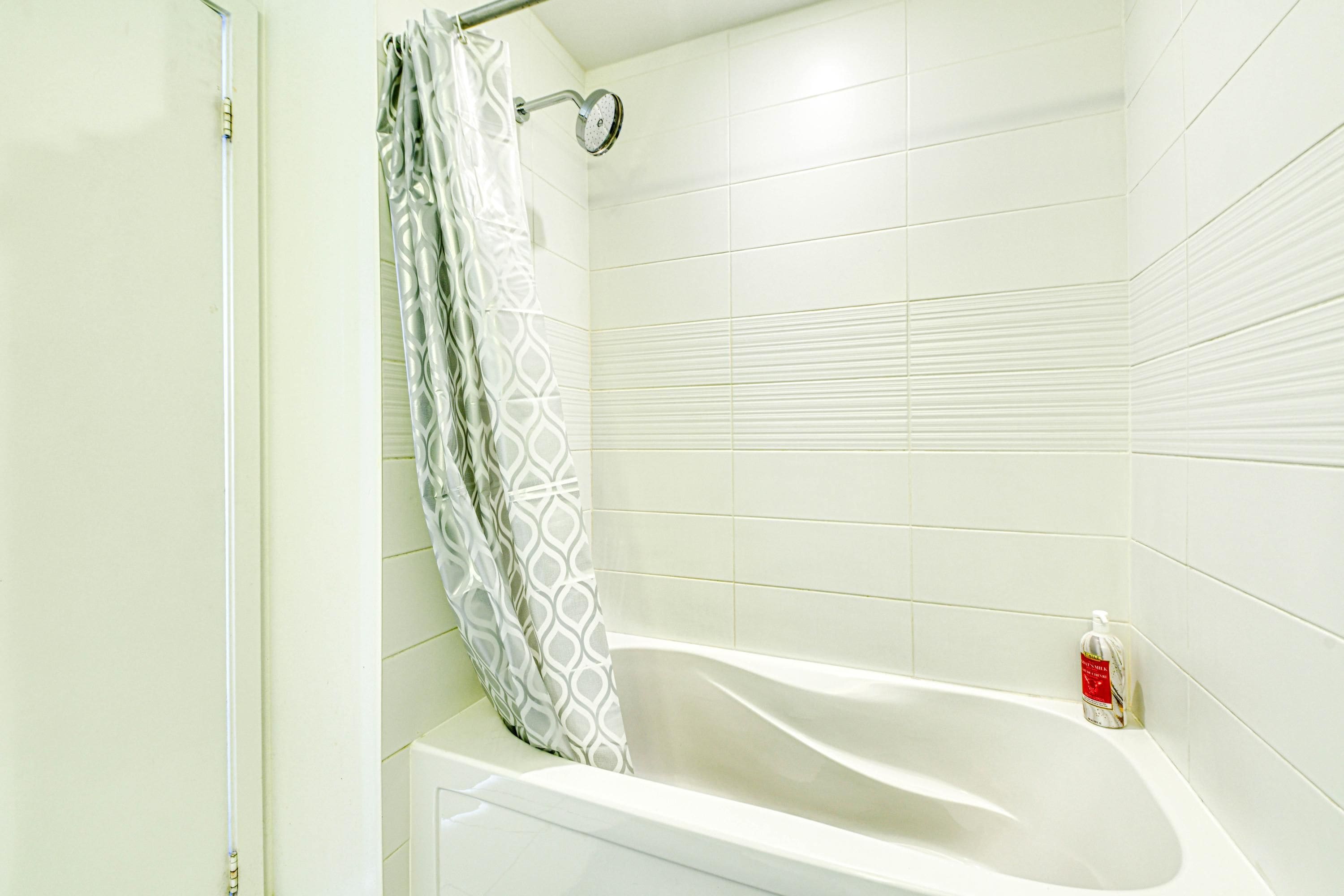 A bathroom with a bathtub, a shower curtain, and a bottle of hand soap on the wall.