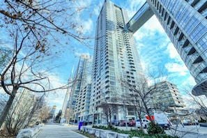 A modern high-rise building with a glass facade, surrounded by leafless trees and parked vehicles. - Panorama Suites-Fort York (Toronto)