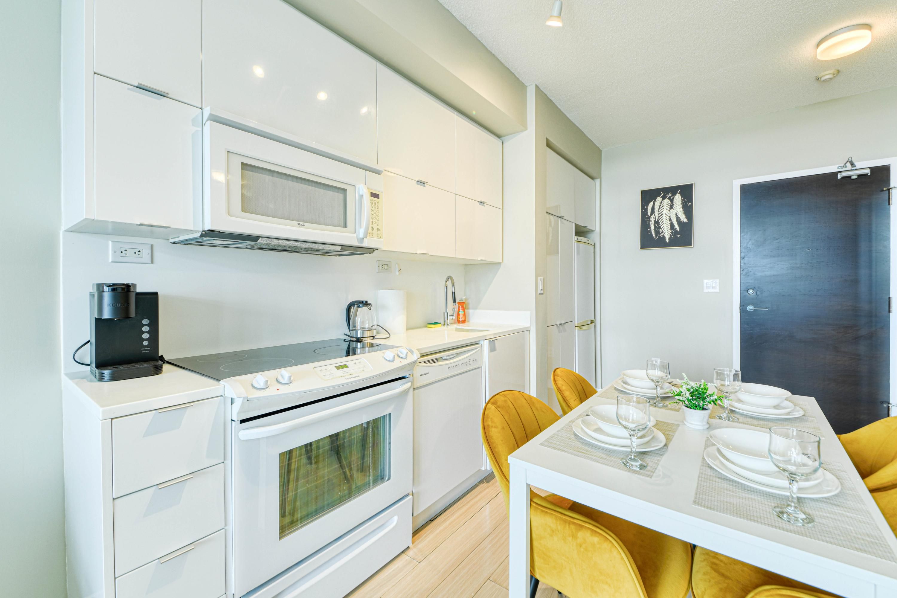 A modern kitchen with white appliances, a dining table set with plates and glasses, and a dark door in the background.