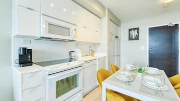 A modern kitchen with white appliances, a dining table set with plates and glasses, and a dark door in the background.
