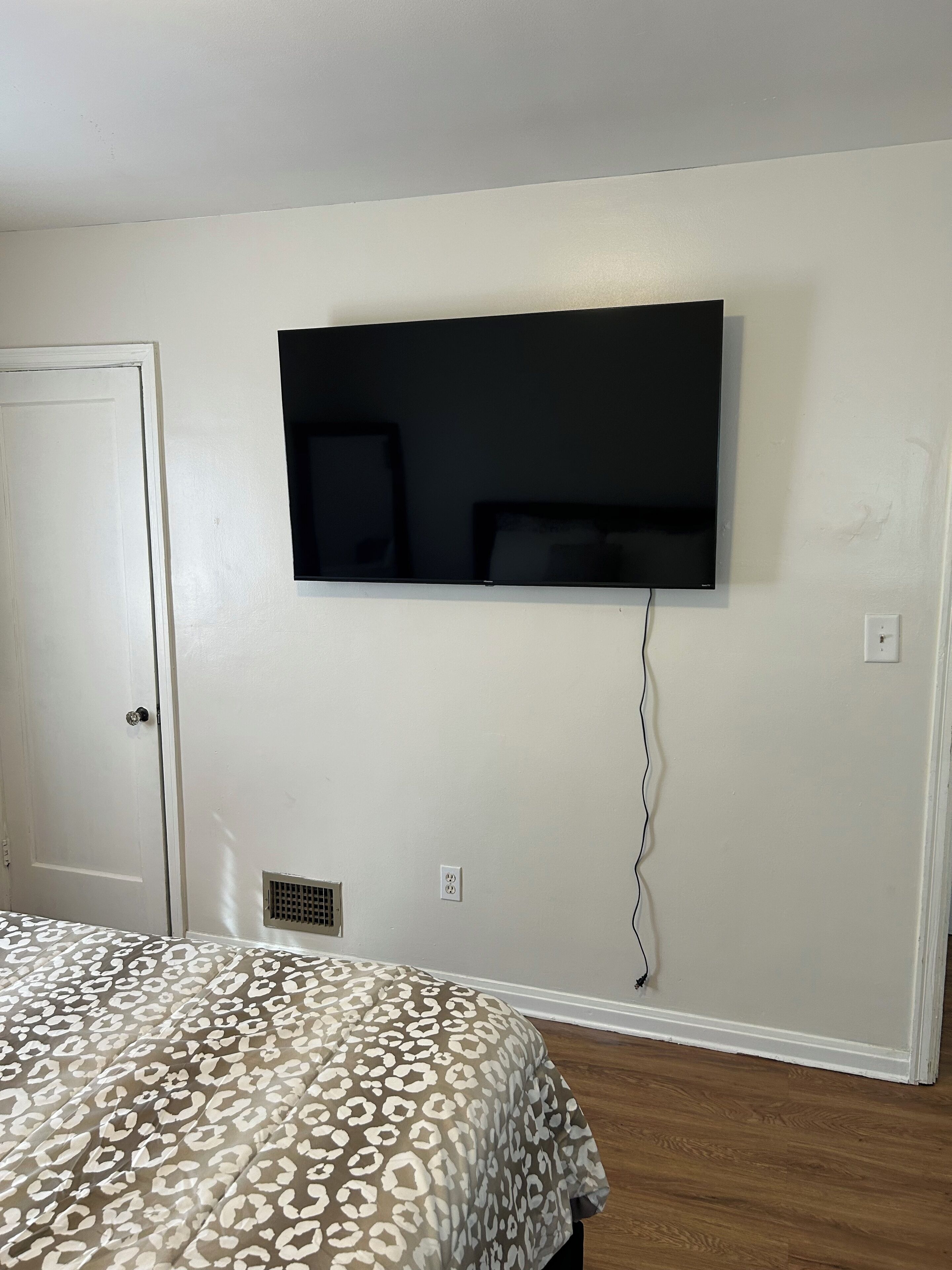 A bedroom with a bed, a television mounted on the wall, a door, and a vent.