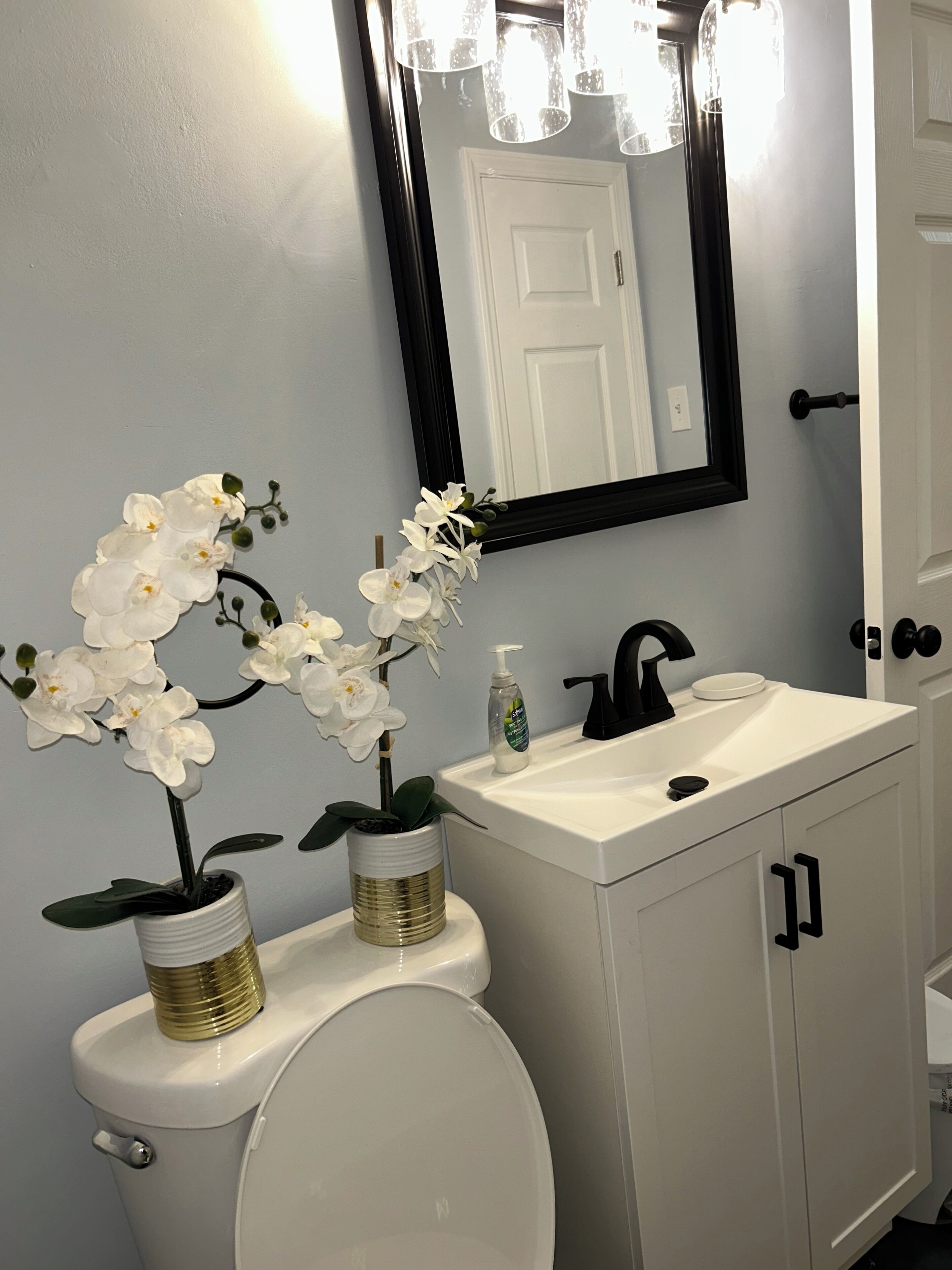 A bathroom with a white toilet, a sink with a black faucet, and two white orchids in gold and white pots.