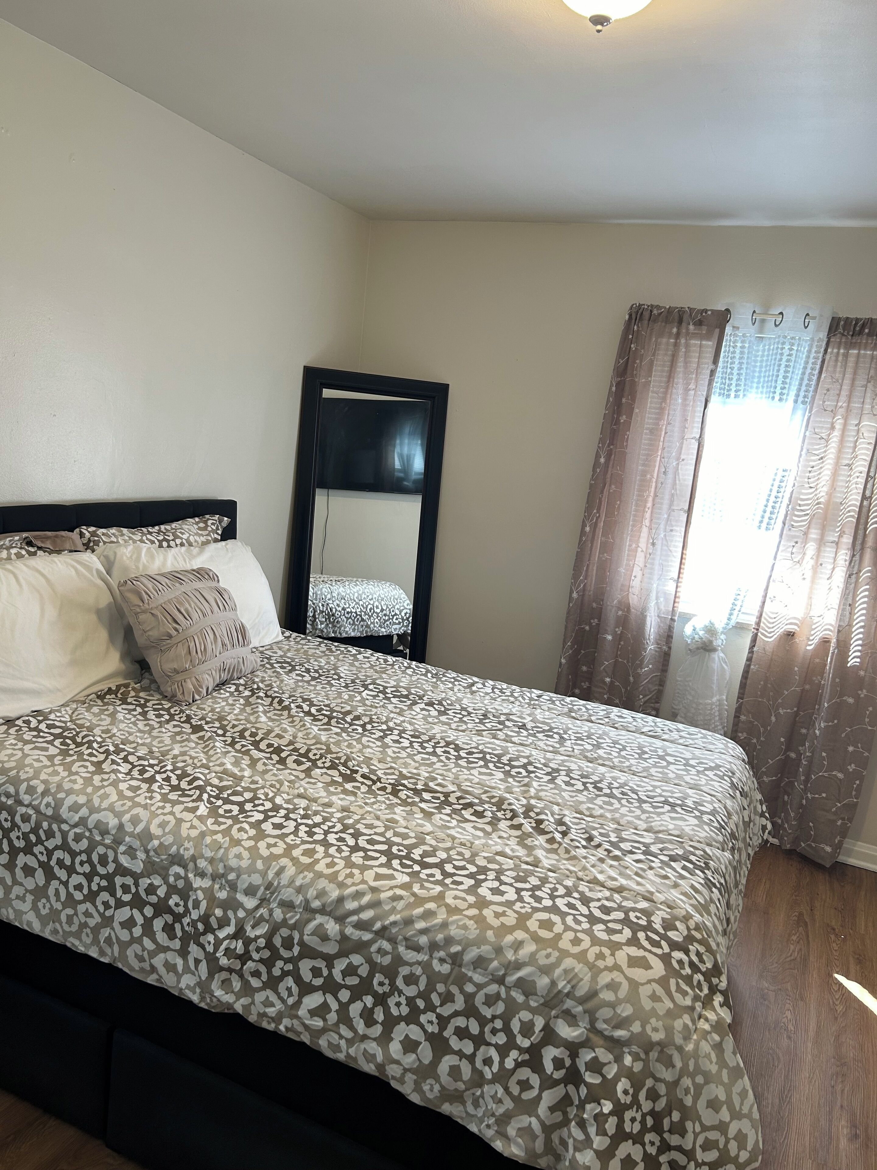 A bedroom with a bed, a mirror, and a window with curtains.