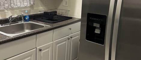 A kitchen with white cabinets, a stainless steel refrigerator, a granite countertop, and a sink.