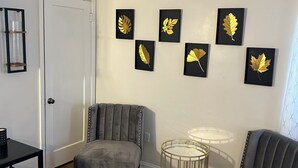 Uma sala de estar com uma poltrona cinza, uma mesinha redonda e uma estante com jogos de tabuleiro.