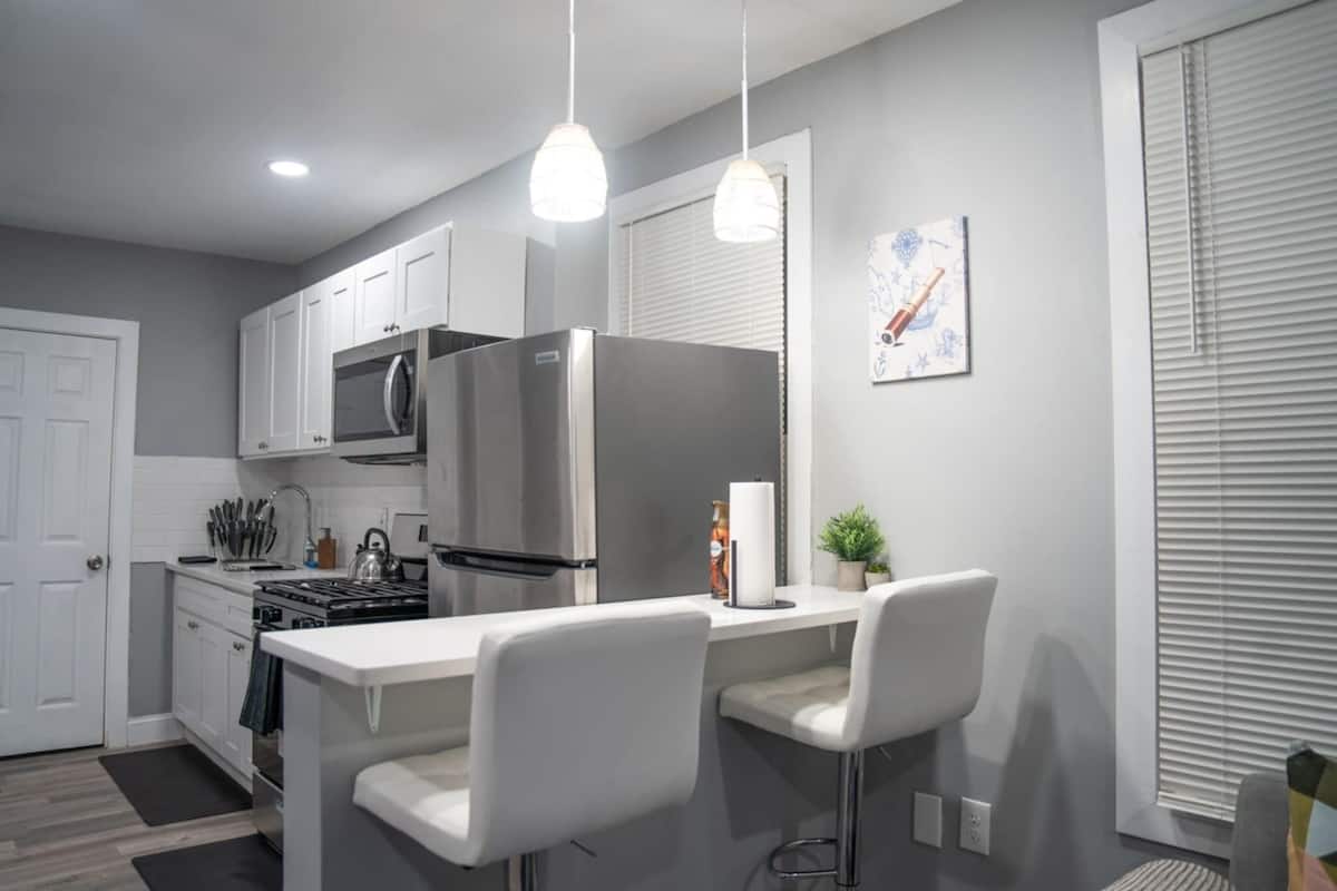 Une cuisine moderne avec des meubles blancs, des appareils en acier inoxydable et un coin bar avec des chaises blanches.